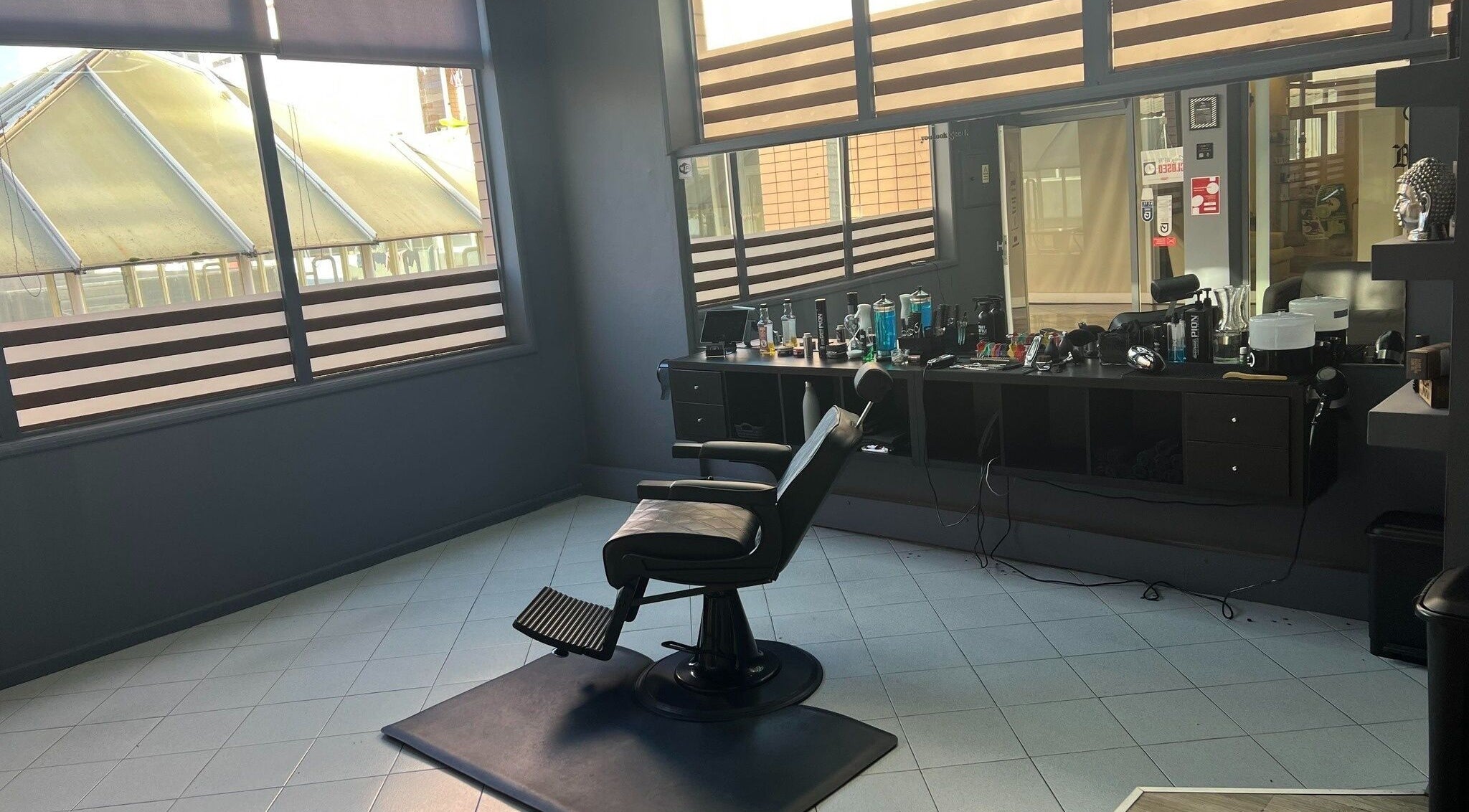 Sala moderna de barbearia no Maus Hábitos, Santo Tirso, Porto, PT, com cadeira e produtos de beleza.