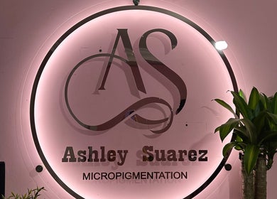 Logotipo iluminado de Ashley Suárez Micropigmentation en Guayaquil, Guayas, EC con fondo rosa y plantas verdes.