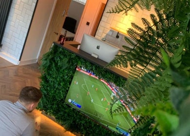 A stylish reception area at Cutthroat Jacks, Stockport, England, GB, featuring lush greenery and a TV showing a game.