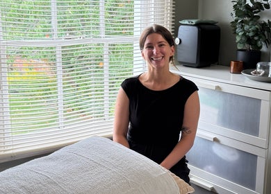 Smiling woman in therapy room at Root and Remedy Wellness, Purleigh, England, GB, beside a massage table.