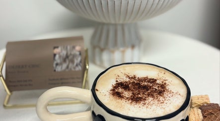 Cup of cappuccino at Desert Chic Hair, Urangan, Queensland, AU. Cozy ambiance with salon card in background.