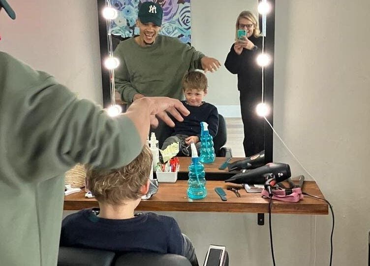 Child enjoys haircut at Barber On Wheels, Gqeberha, Eastern Cape, ZA; stylist and mirror reflections visible.