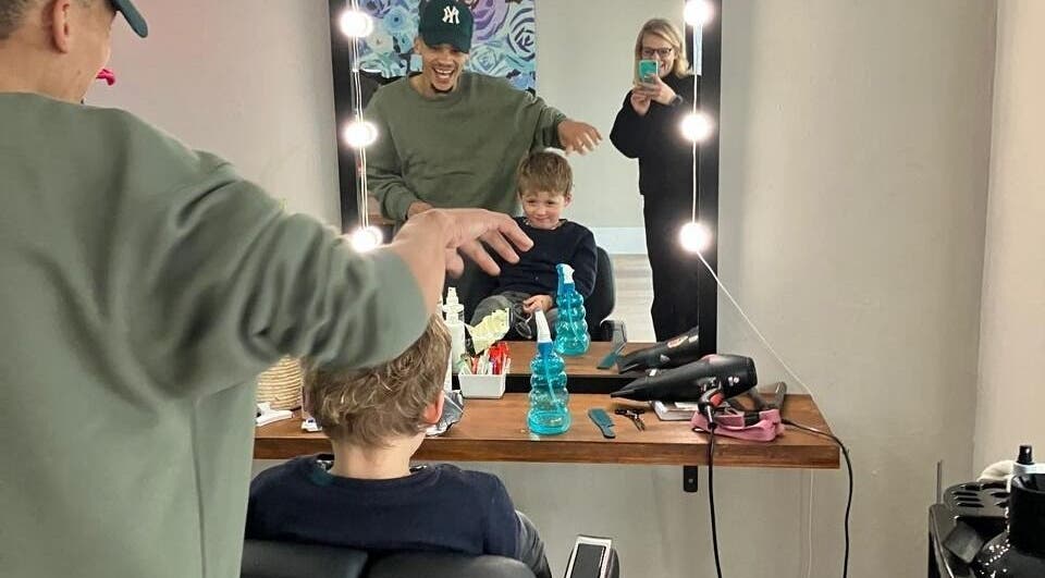 Child enjoys haircut at Barber On Wheels, Gqeberha, Eastern Cape, ZA; stylist and mirror reflections visible.