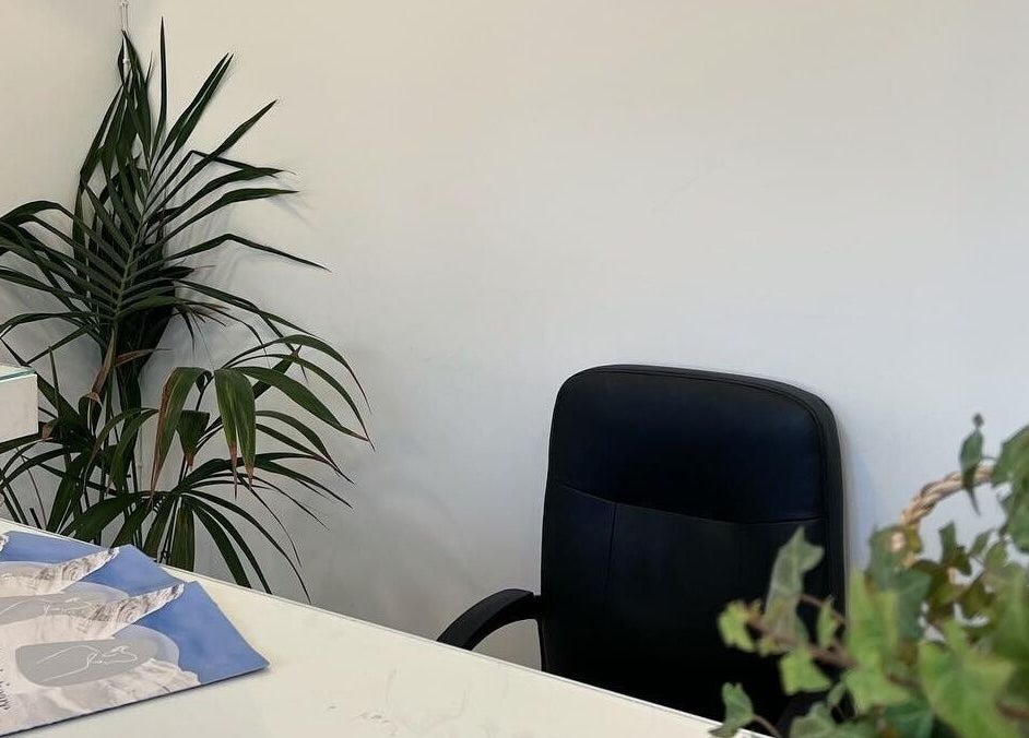 Inviting reception area at Aestheticare, Τριοβάσαλος, GR, featuring a lush potted plant and sleek black chair.