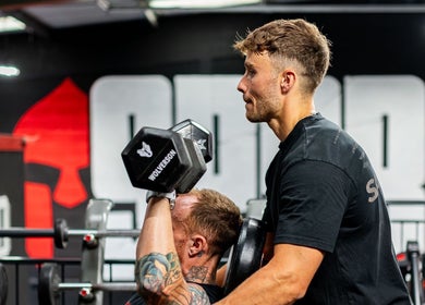 Personal trainer assisting client with dumbbell workout at Jnemzcoaching, Wellington, England, GB.