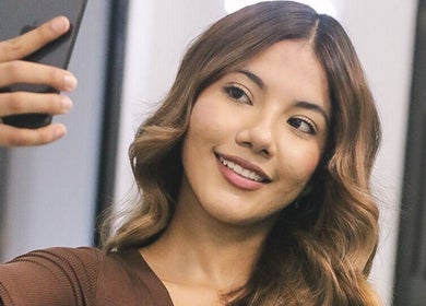 Cliente sonriendo en Kate Karlsson, Cabañas, Cabañas, SV, con cabello y maquillaje impecables.