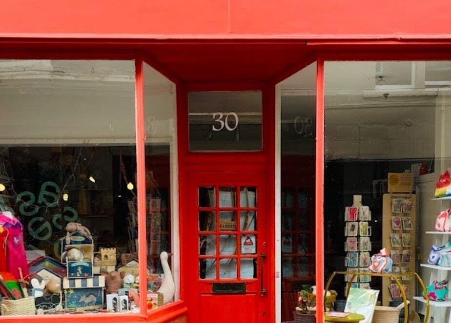 Front view of TULA AYURVEDA's inviting red façade storefront in Frome, England, GB, showcasing wellness products.