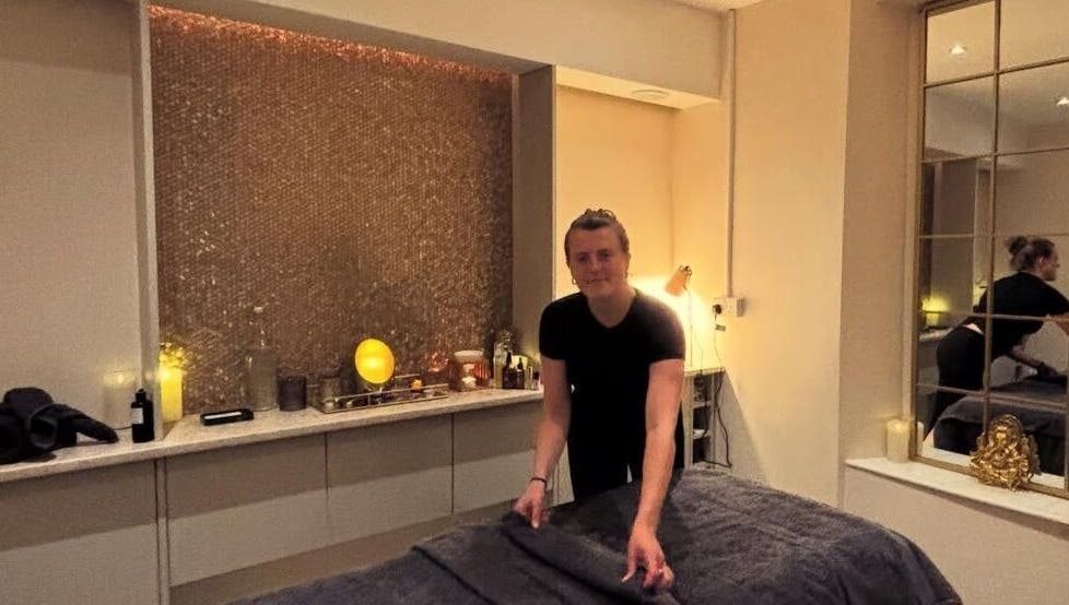 Therapist prepares a relaxing room at Tula Ayurveda, Frome, England, GB, featuring warm lighting and decor.