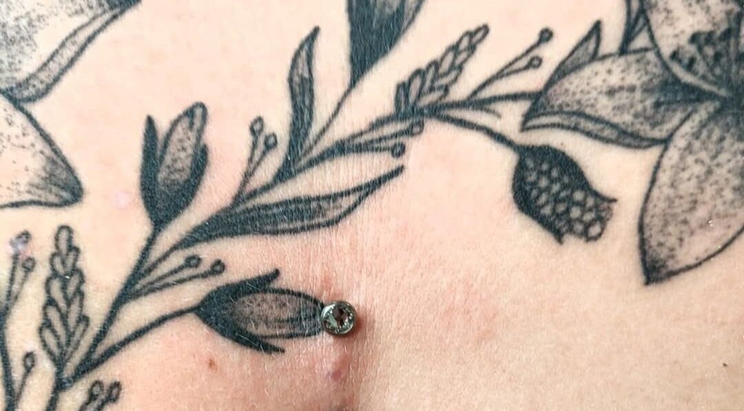 Floral tattoo with dermal piercing at Elysian Beauty and Piercing in Sudbury, GB.