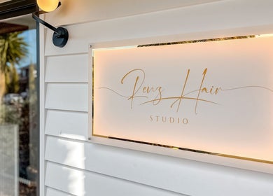 Illuminated sign of Renz Hair Studio at Melbourne, Victoria, AU on bright exterior wall.