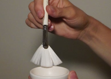 A hand holding a brush over a bowl at The Luxe Hair Spa, Barcelona, Catalunya, ES.
