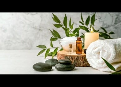 Spa essentials at Simply Luxe Beauty in Coatbridge, Scotland, GB, featuring stones, towel, candle, and foliage.