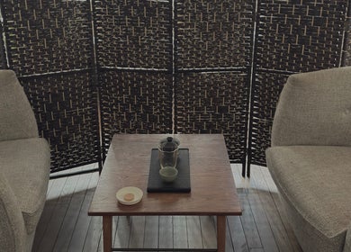 Relaxing seating area at Alchème Sanctuary, London, England, GB with woven divider and a wooden table.