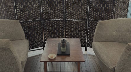Relaxing seating area at Alchème Sanctuary, London, England, GB with woven divider and a wooden table.