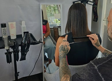 A stylist cuts hair at Cuts by Luke, Croydon, England, GB, with styling tools on a stand.