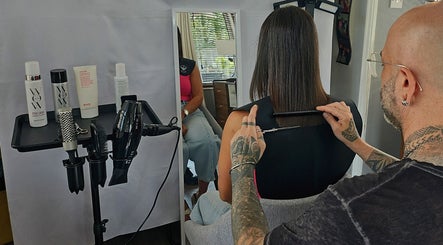 A stylist cuts hair at Cuts by Luke, Croydon, England, GB, with styling tools on a stand.