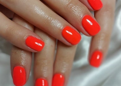 Bright red manicured nails at Tynaesthetics_ in London, England, GB on a satin background.