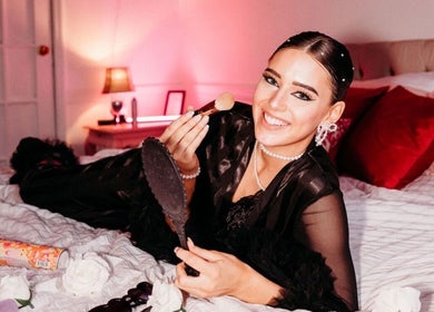 Smiling woman with makeup brush at B. Hive Salon in Huntsville, Alabama, US, surrounded by beauty essentials.