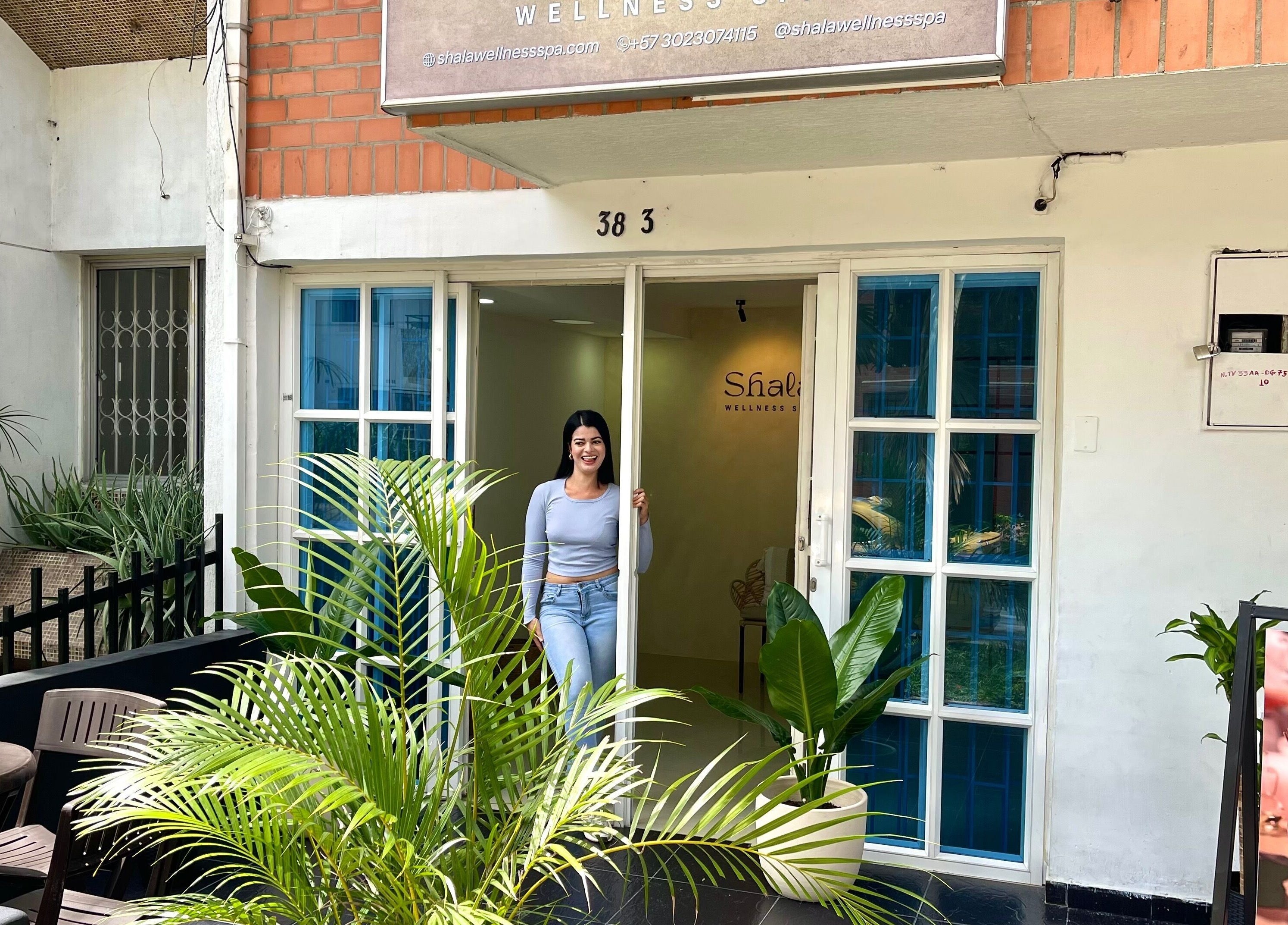 Entrada de Shalá Wellness Spa en Medellín, Antioquia, CO con puertas abiertas y plantas enmarcando la entrada.