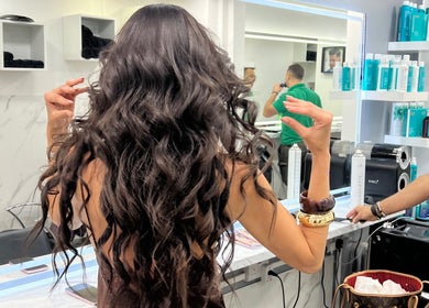 Woman styling voluminous hair at The Royal Salon in London, England, GB. Modern interior and hair products visible.