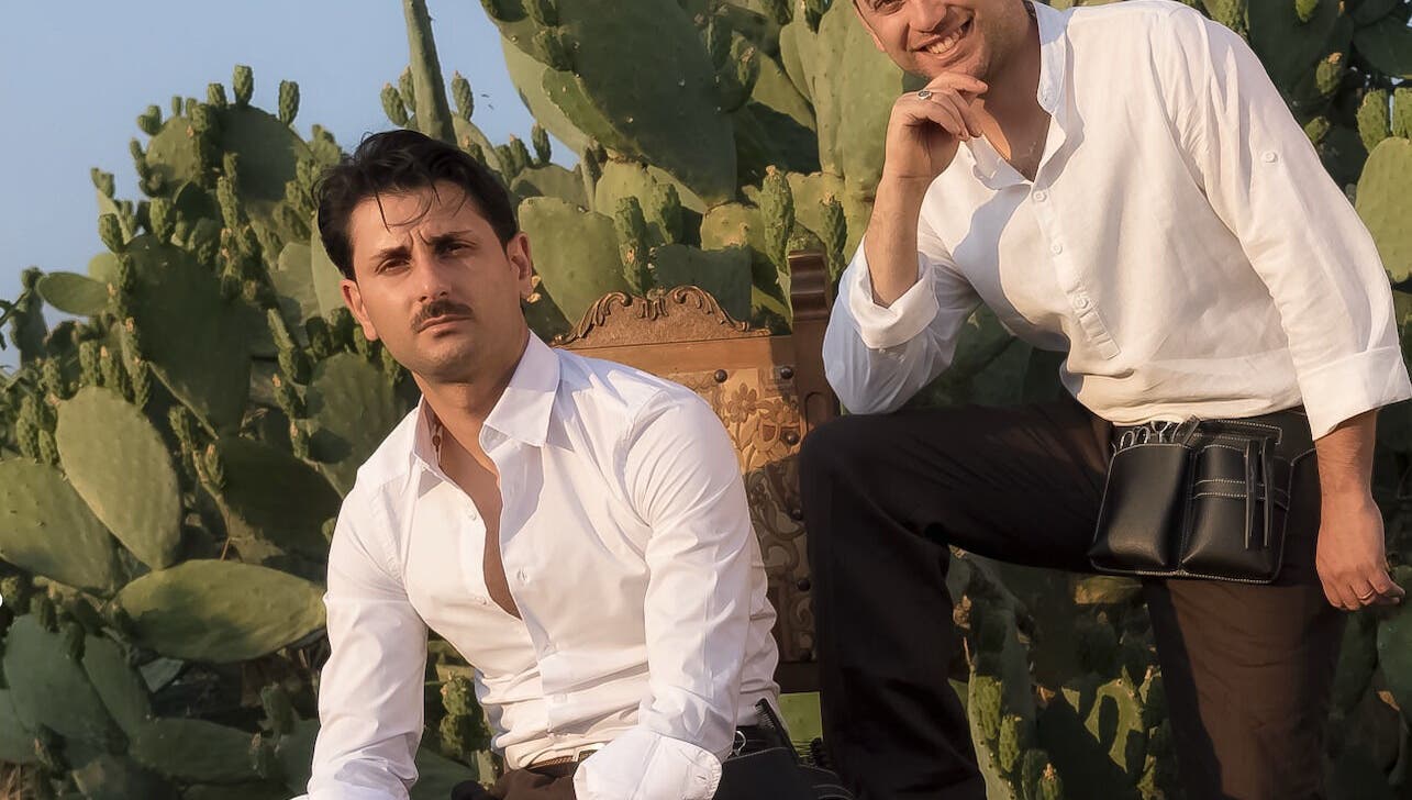 Due stilisti di Gioele & Enrico Salon a Paternò, Sicilia, IT, seduti davanti a un fondale di cactus.