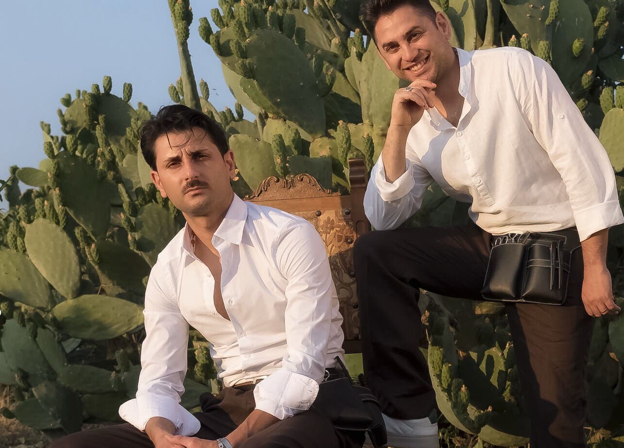 Due stilisti di Gioele & Enrico Salon a Paternò, Sicilia, IT, seduti davanti a un fondale di cactus.