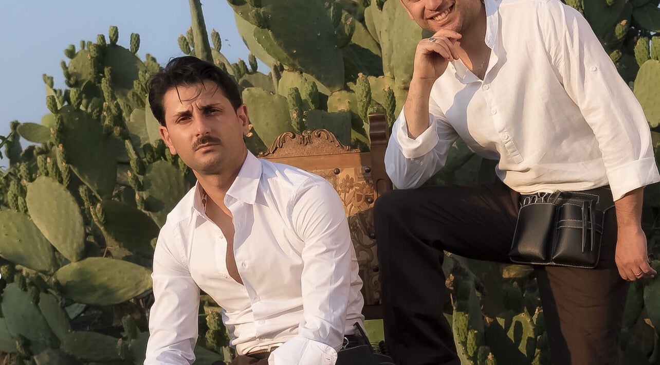 Due stilisti di Gioele & Enrico Salon a Paternò, Sicilia, IT, seduti davanti a un fondale di cactus.