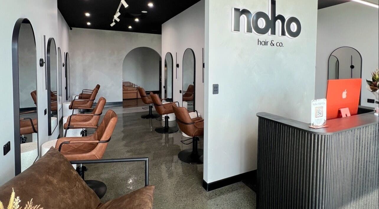 Modern interior of Noho Hair & Co. in Ormeau, Queensland, AU, featuring stylish salon chairs and a sleek reception desk.