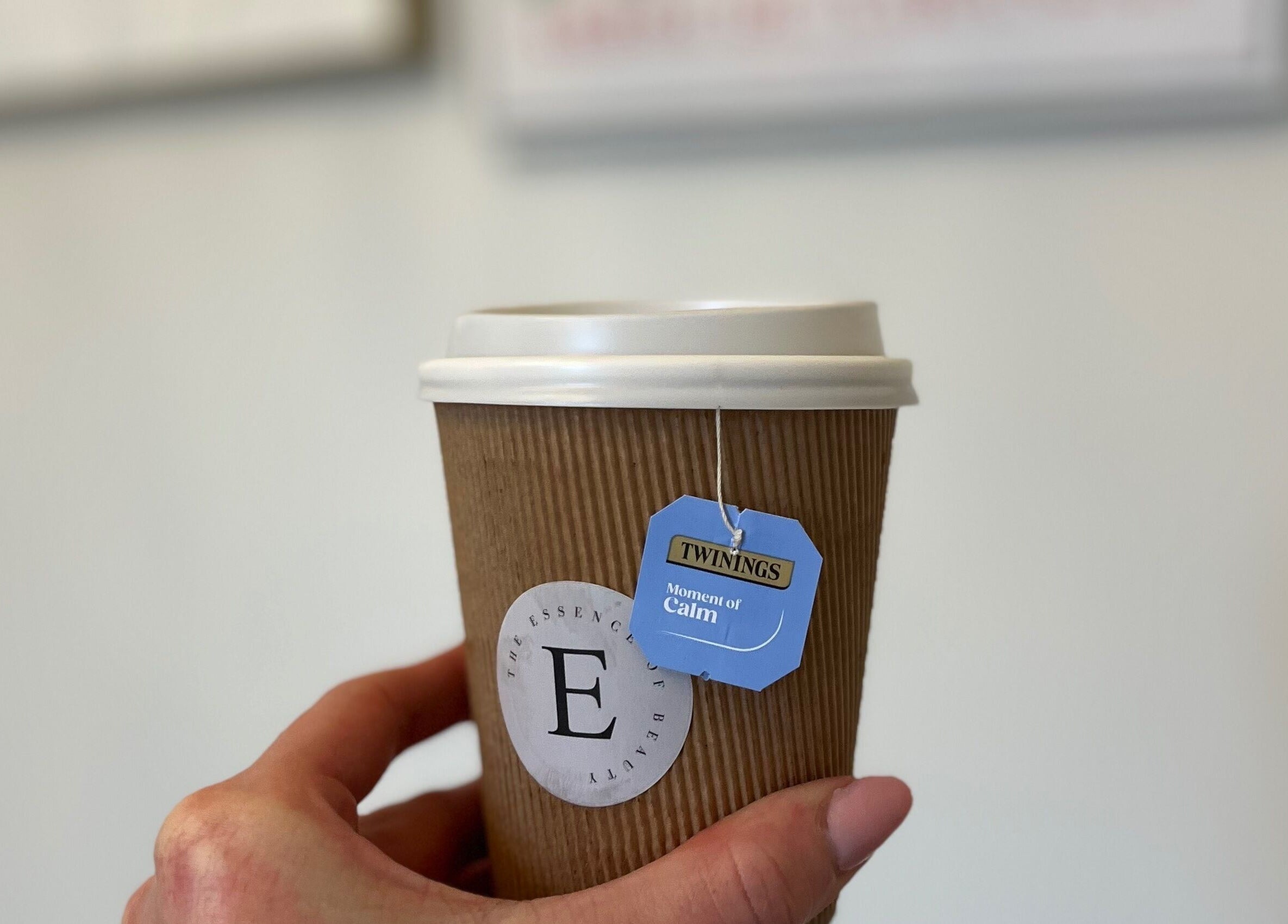 A hand holds a branded cup of tea at The Essence Of Beauty in Chatburn, England, GB, promoting relaxation.