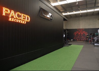 Paced Recovery gym interior with neon sign in Melbourne, Victoria, AU. Modern fitness equipment is visible.