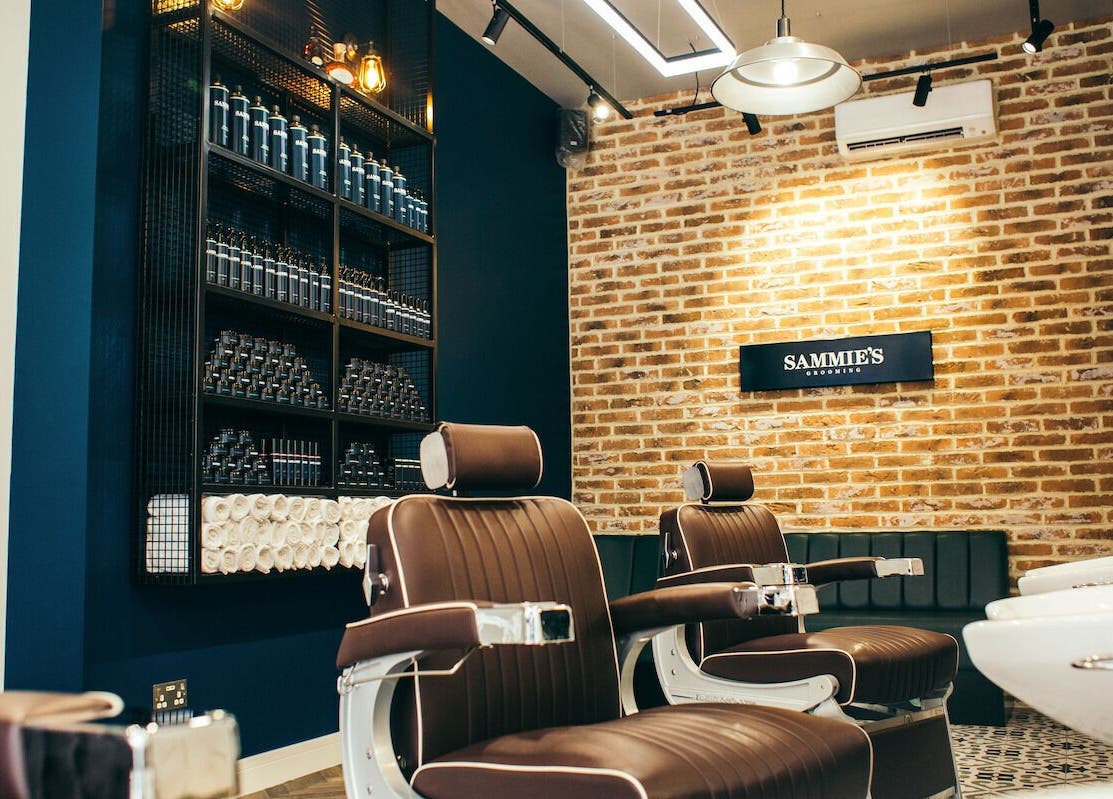 Chic barber chairs at Sammies Studio - Fulham Road, London, England, GB with brick wall and product shelves.
