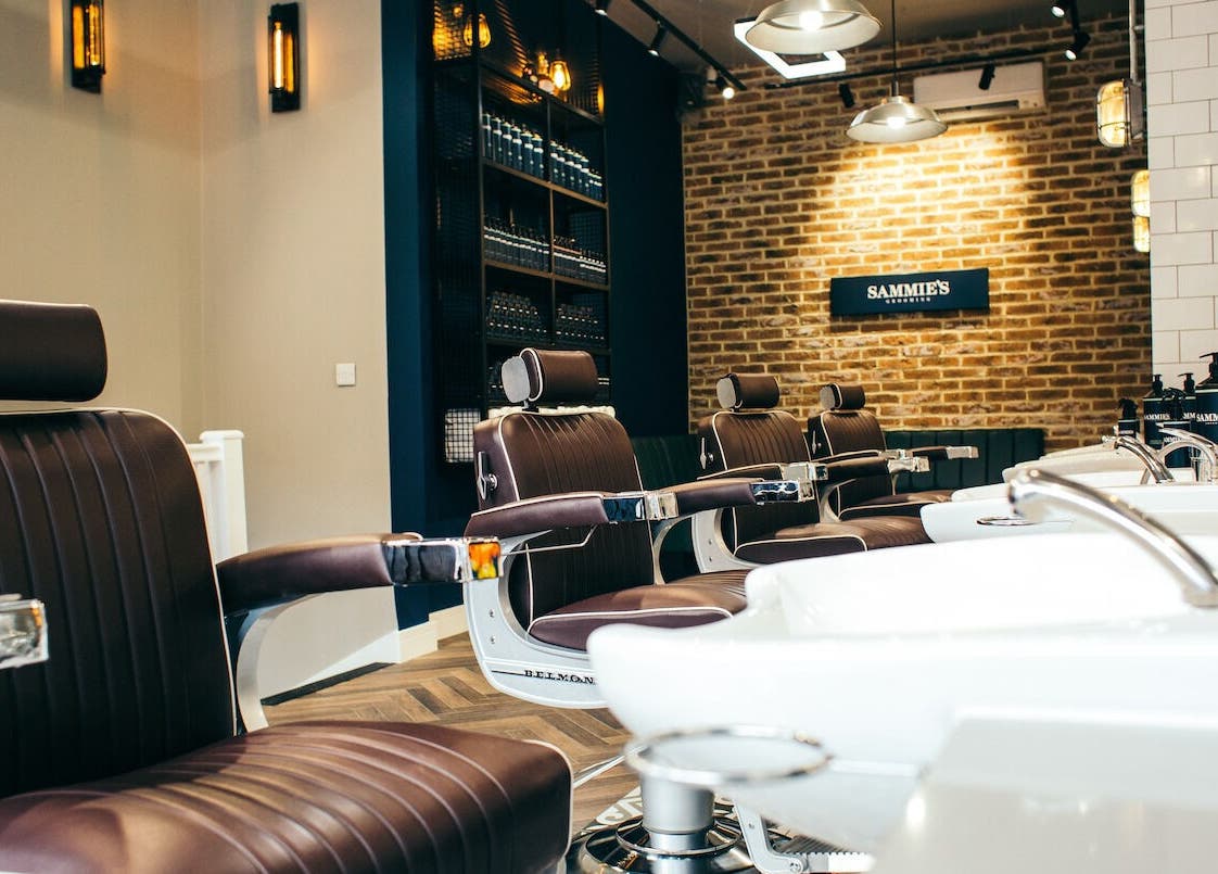 Modern barber chairs in Sammies Studio - Fulham Road, London, England, GB with brick wall backdrop.