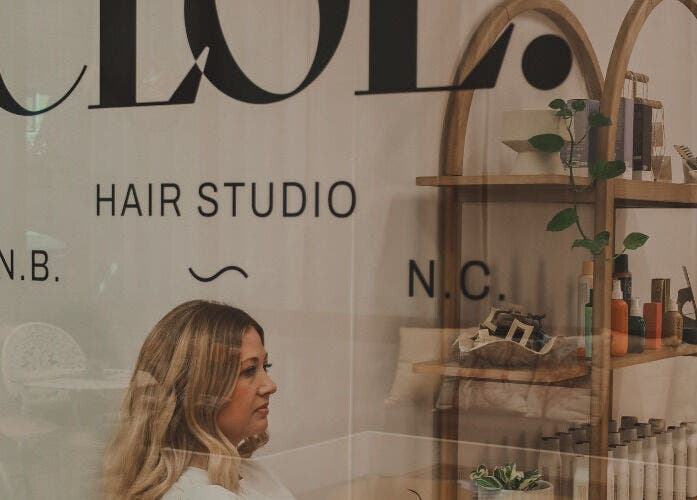 Woman inside Cloe. Hair Studio in Woolgoolga, New South Wales, AU, next to natural product shelves.