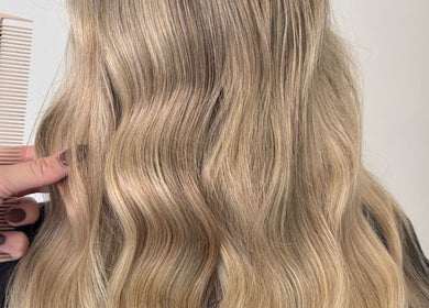 Blonde wavy hairstyle at Hair by Emma Sturt, Beenleigh, Queensland, AU with a stylist combing through.