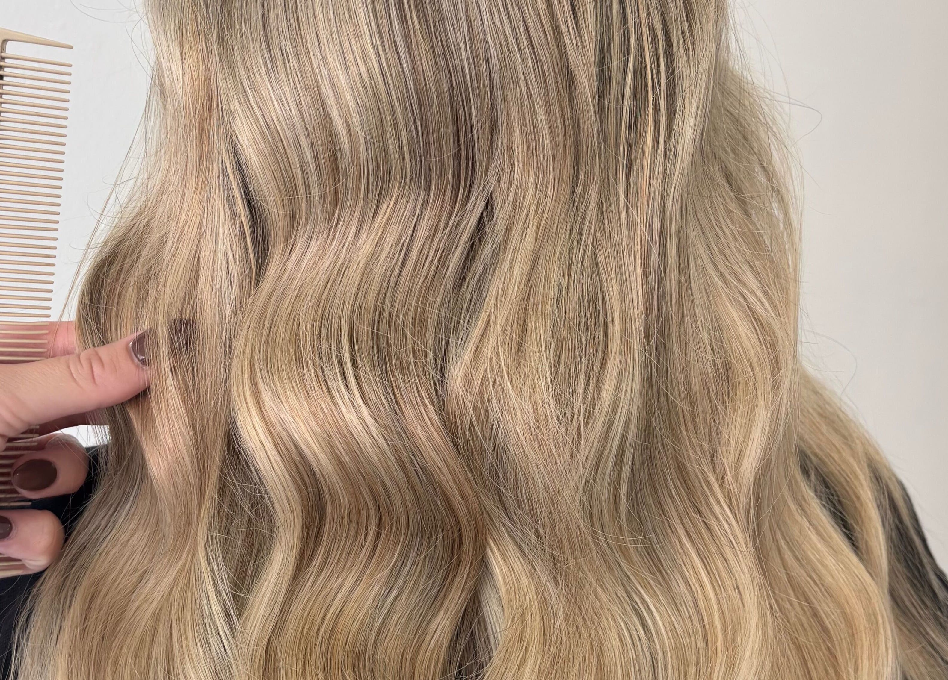 Blonde wavy hairstyle at Hair by Emma Sturt, Beenleigh, Queensland, AU with a stylist combing through.