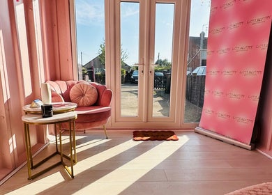 Cozy pink seating area with branded backdrop at Doll Beauty Aesthetics & Training Academy, Cleeve, England, GB.