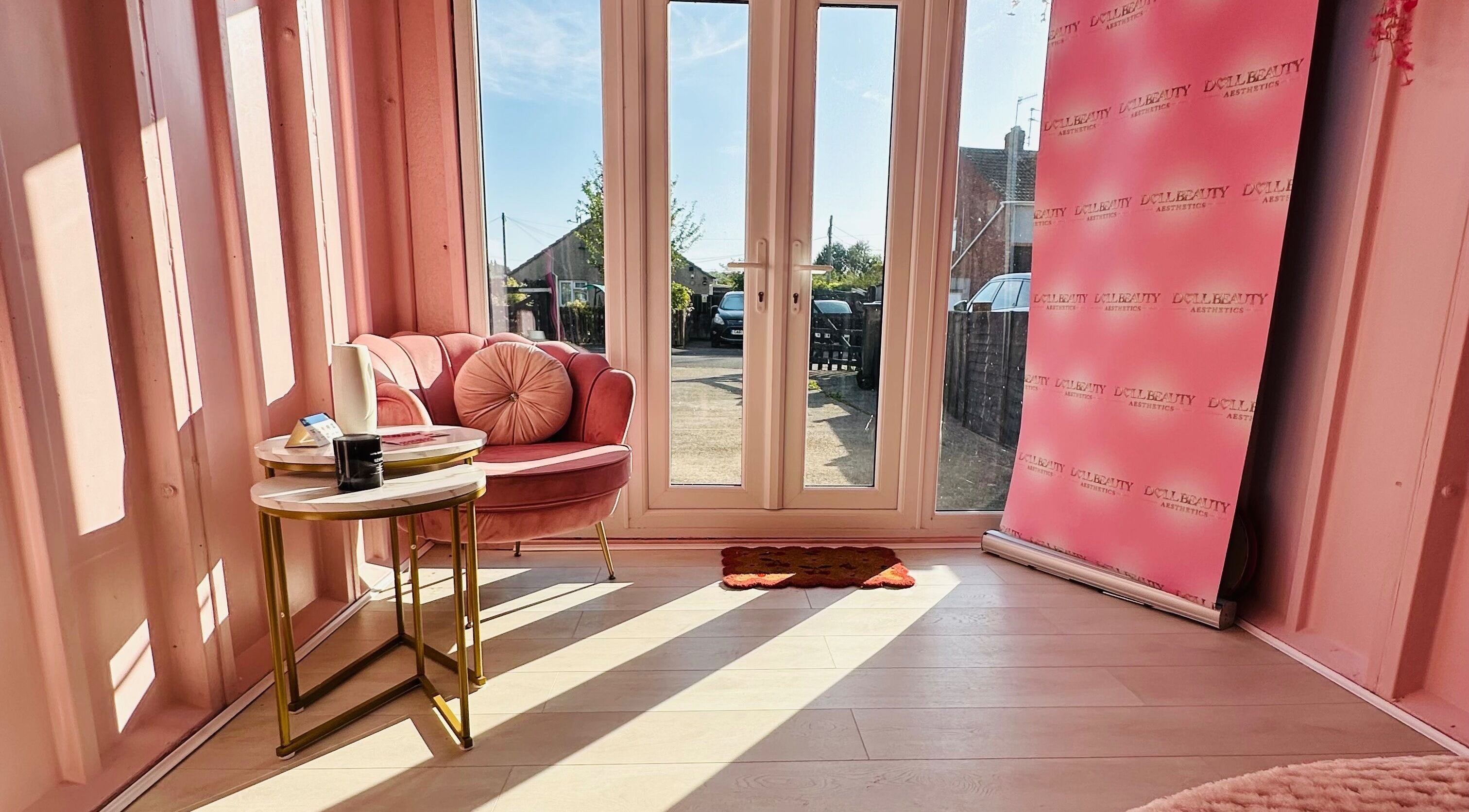 Cozy pink seating area with branded backdrop at Doll Beauty Aesthetics & Training Academy, Cleeve, England, GB.