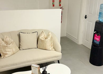Elegant lounge area at Naked Beauty, North Weald Bassett, England, GB showcasing a plush sofa and water cooler.