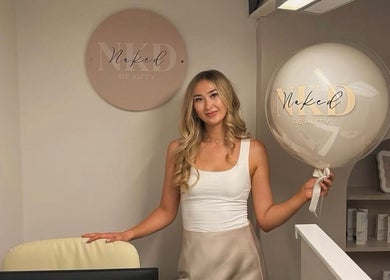 Staff member at Naked Beauty in North Weald Bassett, GB, holding a branded balloon at the welcoming area.