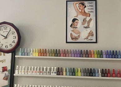 Colorful nail polish display at Oi Nha Trang Spa, Nha Trang, Khánh Hòa, VN, under a clock and beauty poster.