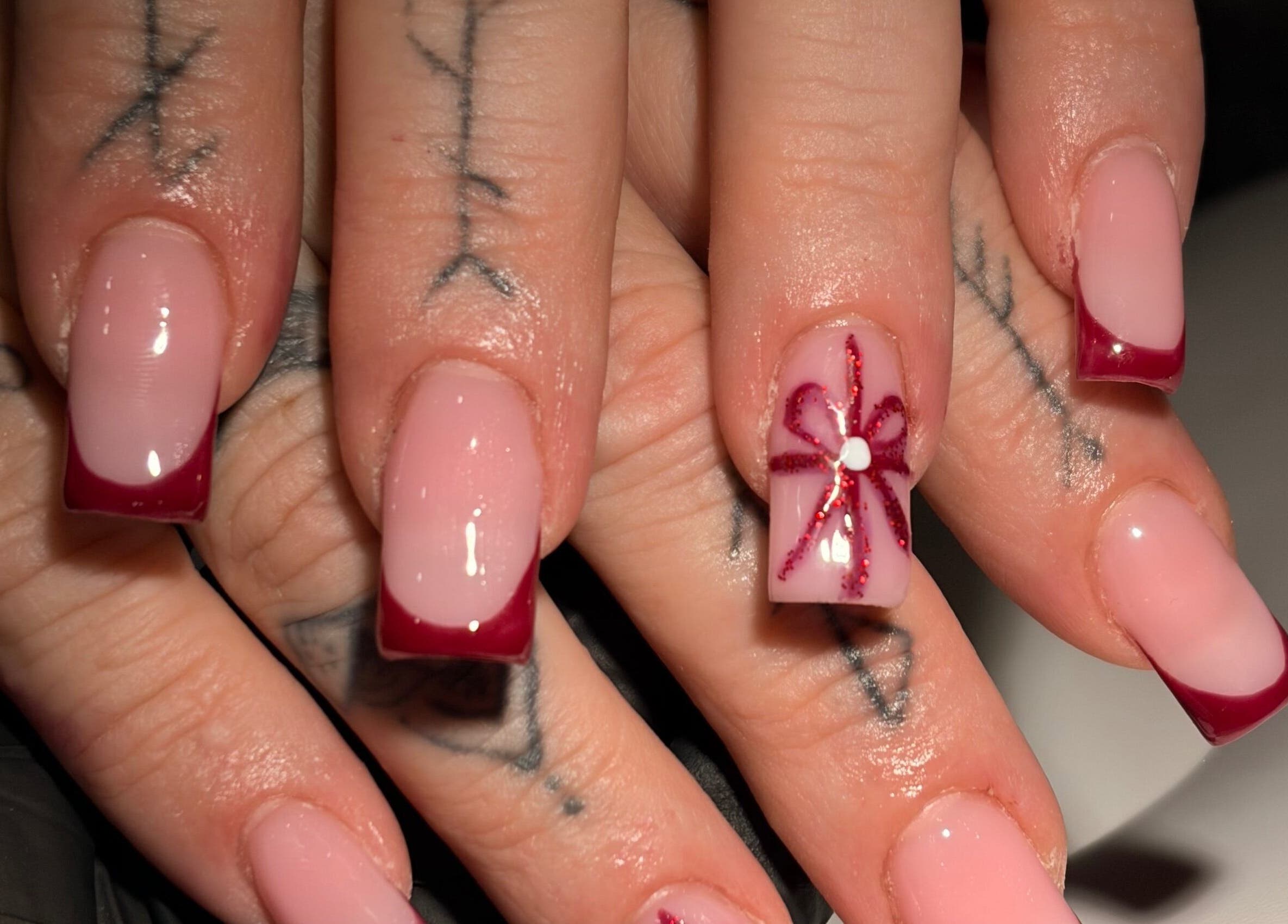 Elegant nail art with red tips and flower design at Niamh&Co, Stanford-le-hope, England, GB.