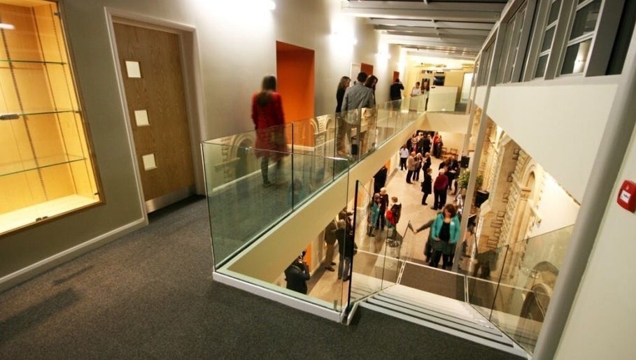 Guests interacting in the modern atrium of True Circle, Oxford, England, GB. Elegant glass railings and spacious design.