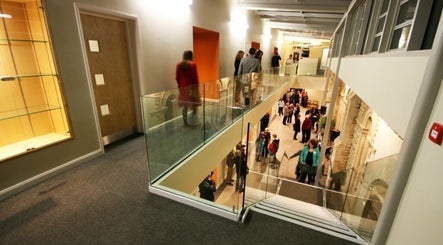 Guests interacting in the modern atrium of True Circle, Oxford, England, GB. Elegant glass railings and spacious design.