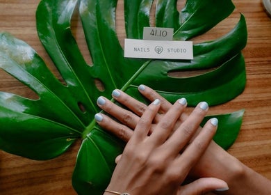 Manos con manicura sobre hoja verde en 41.10 Nails Studio, Tulum, Quintana Roo, MX.