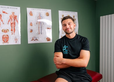 Therapist at Recovery Clinic in Winlaton, England, GB, sitting in front of anatomy posters.