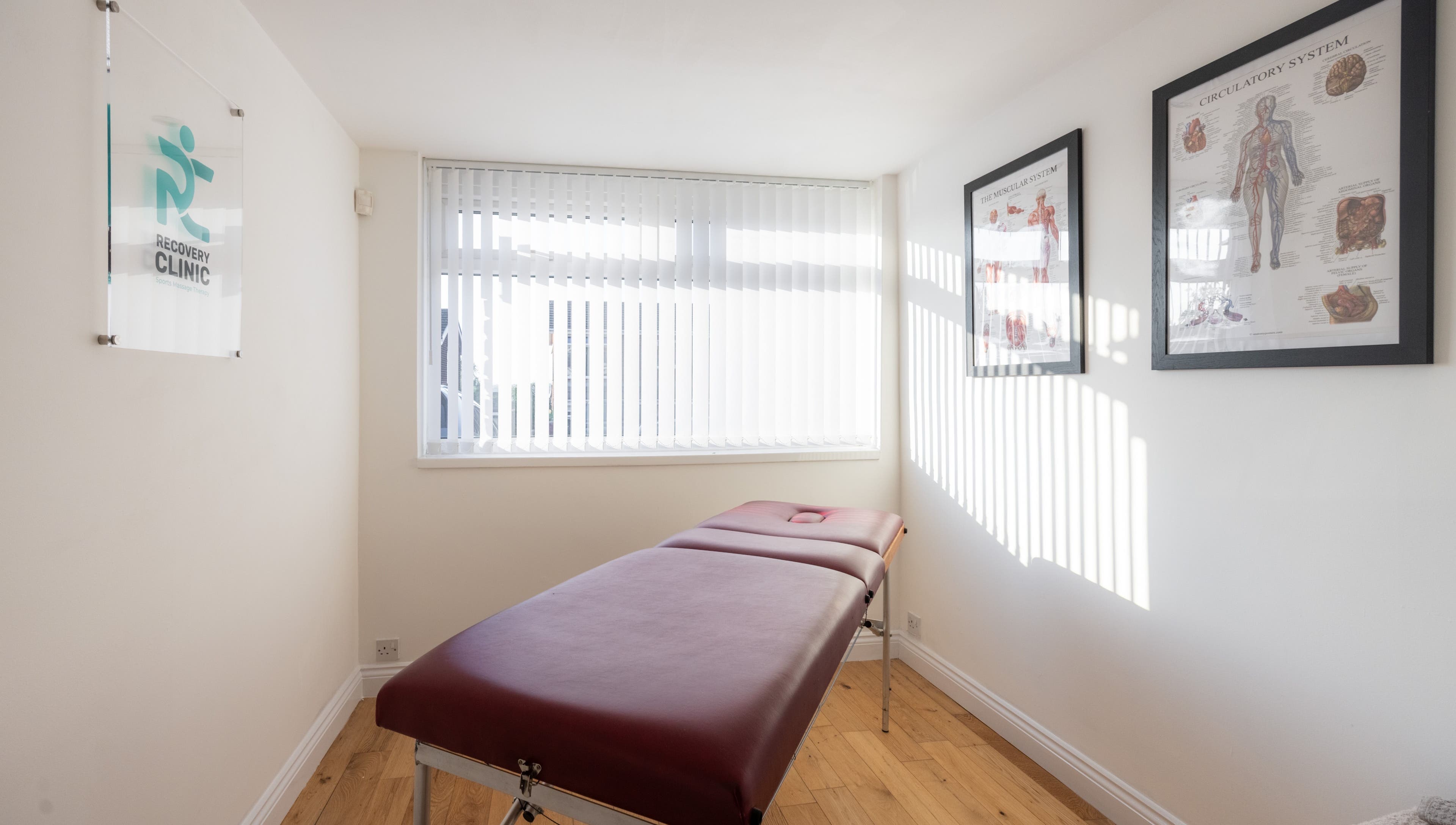 Tranquil treatment room at Recovery Clinic, Winlaton, England, GB, featuring a massage table and anatomical charts.