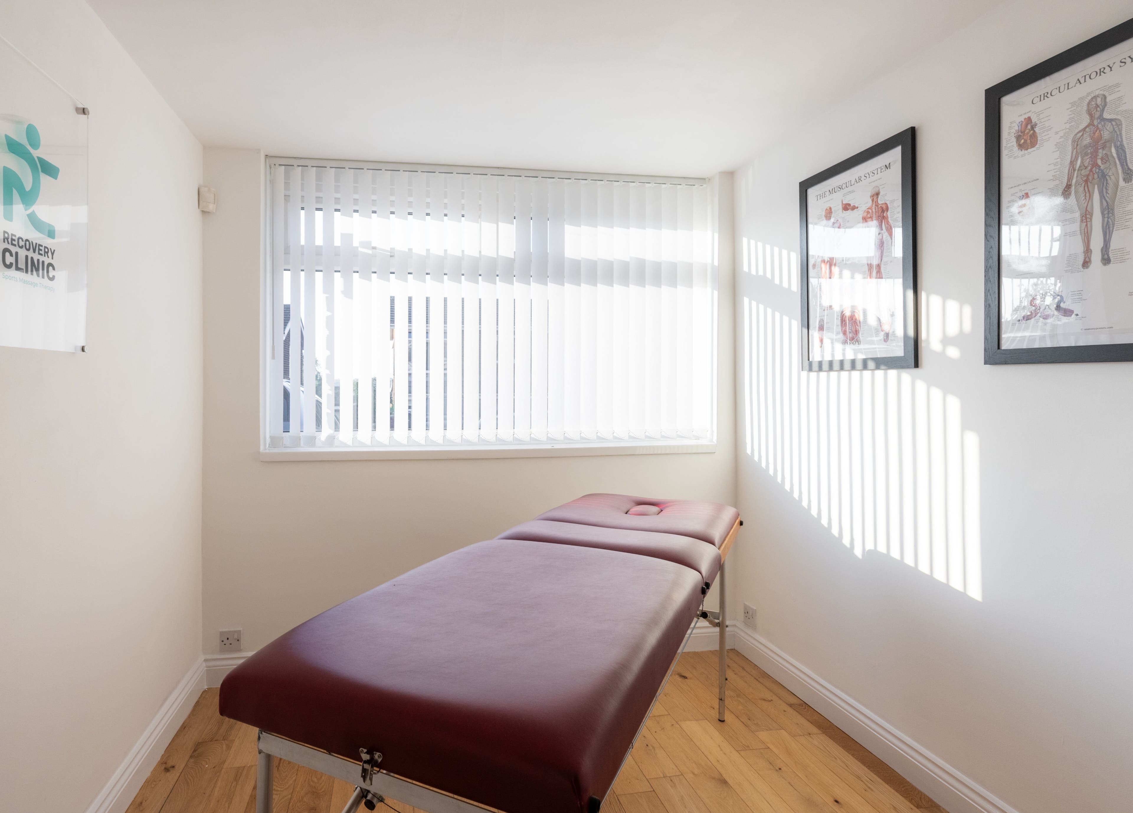 Tranquil treatment room at Recovery Clinic, Winlaton, England, GB, featuring a massage table and anatomical charts.