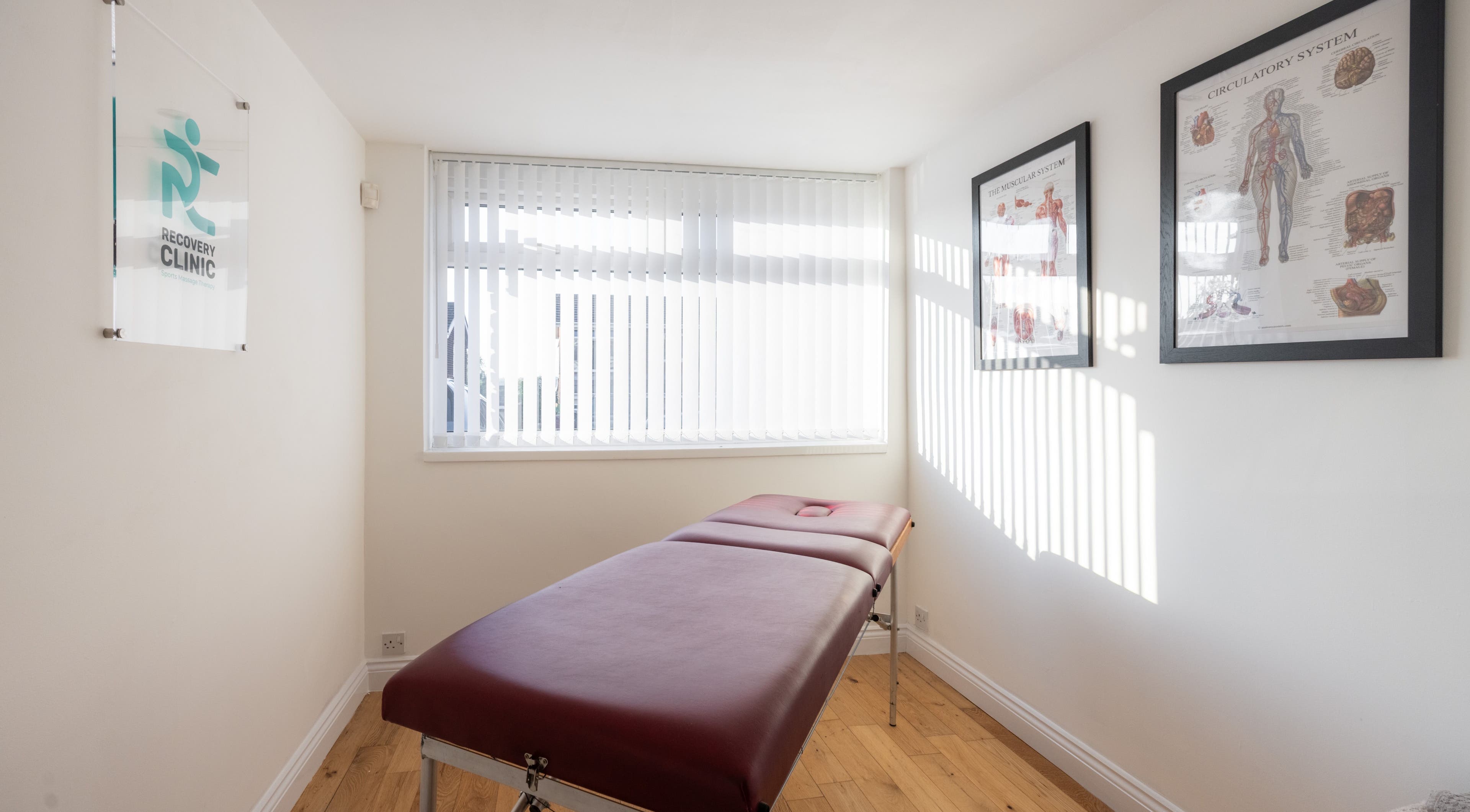 Tranquil treatment room at Recovery Clinic, Winlaton, England, GB, featuring a massage table and anatomical charts.