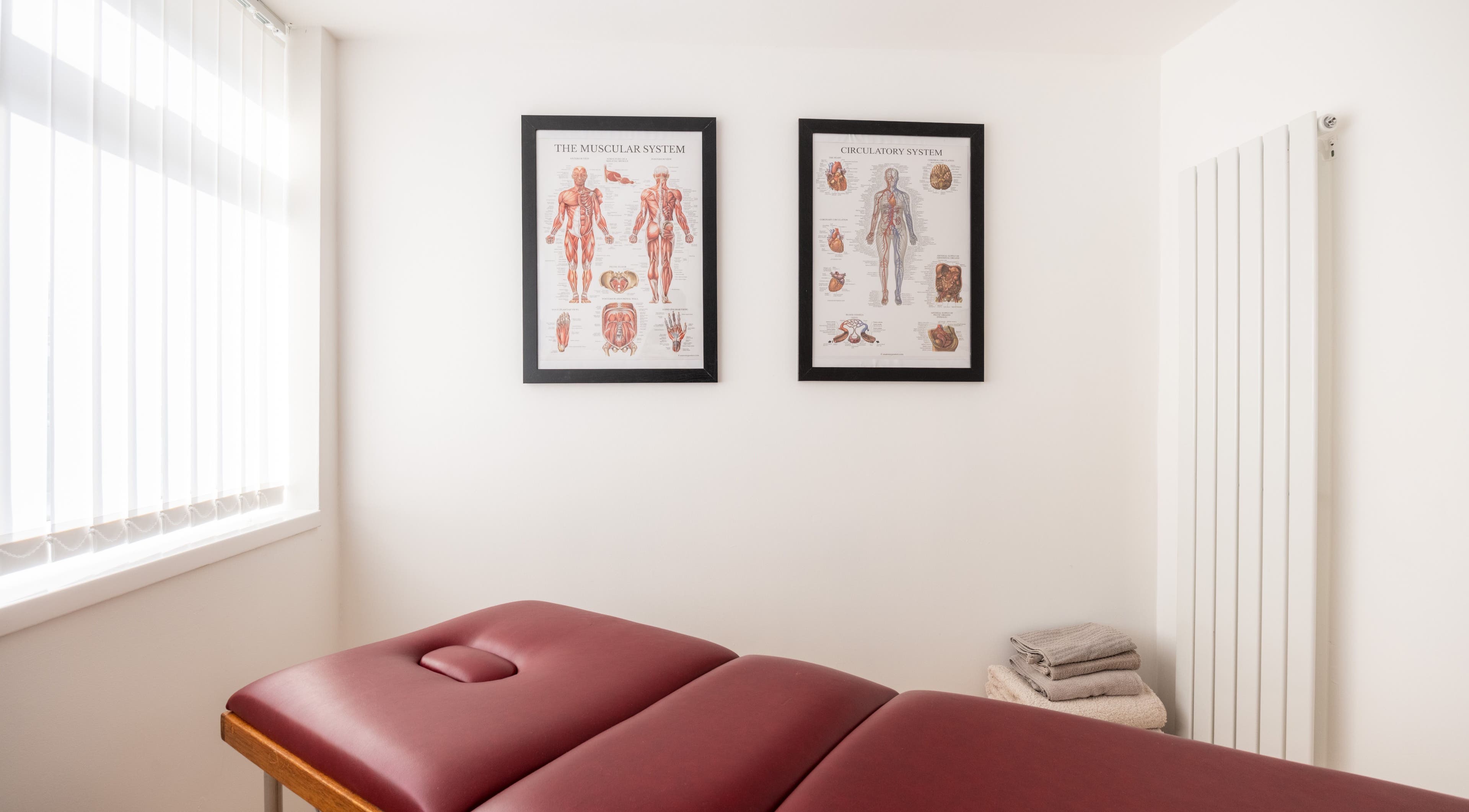 Calm therapy room at Recovery Clinic, Winlaton, England with massage bed and anatomical charts.