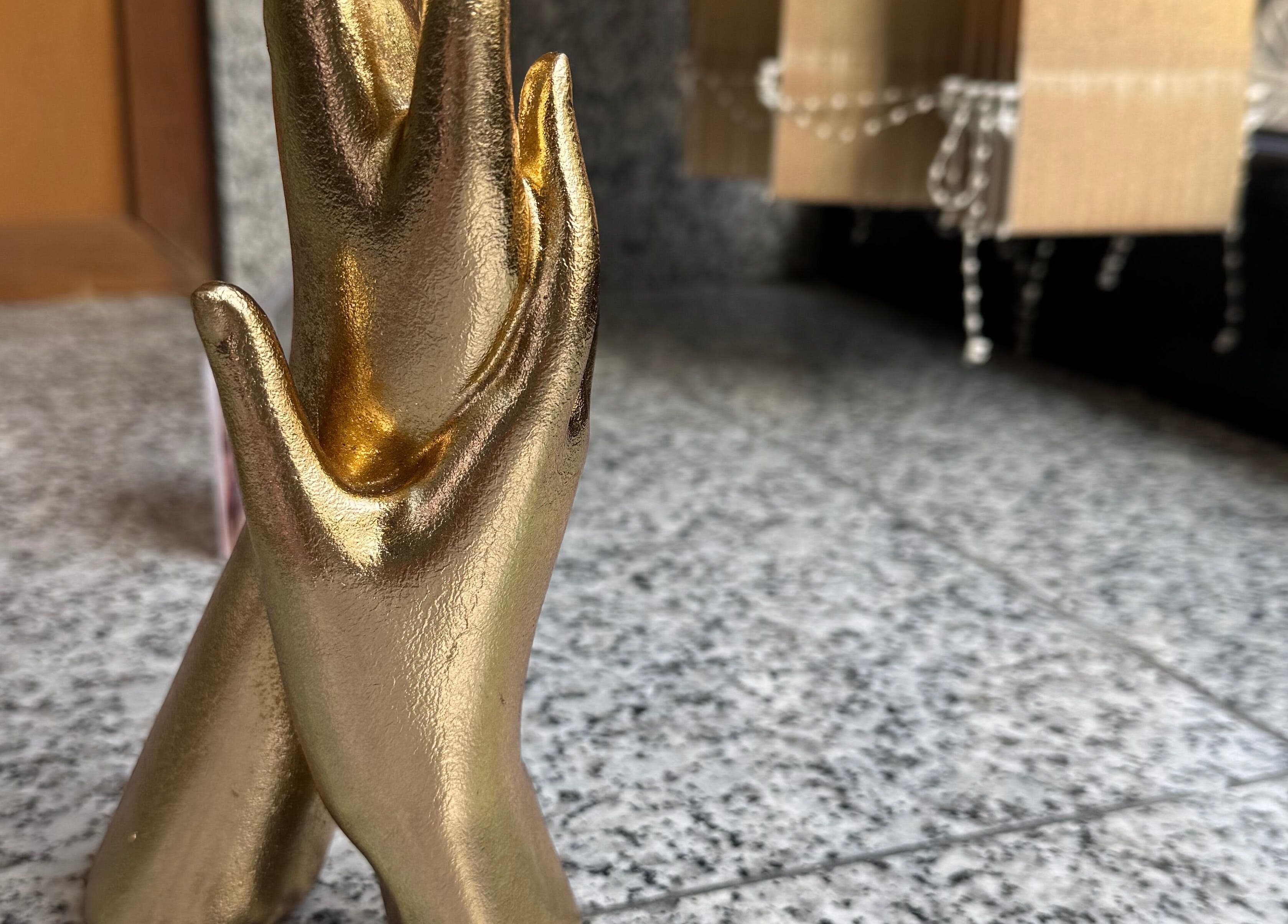 Escultura dourada de mãos entrelaçadas em Karen Passos, Algés, Lisboa, PT.